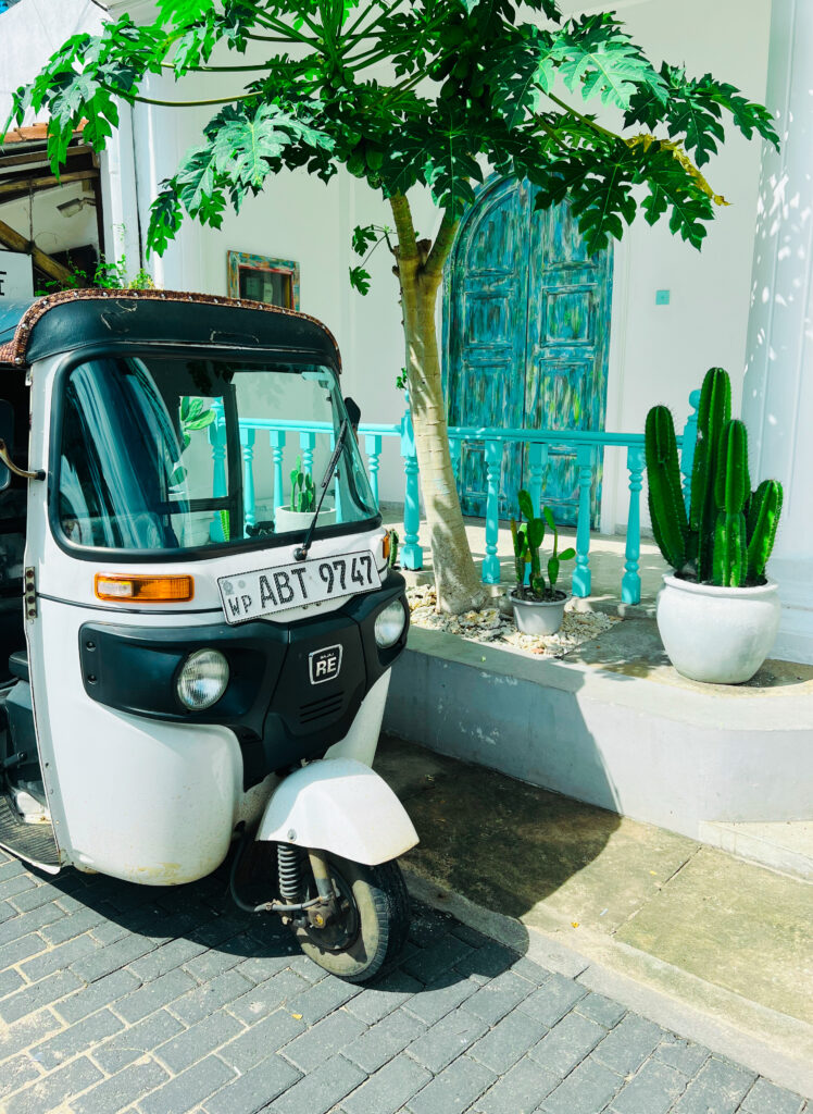 A picture of white tuktuk in front of a blue old building