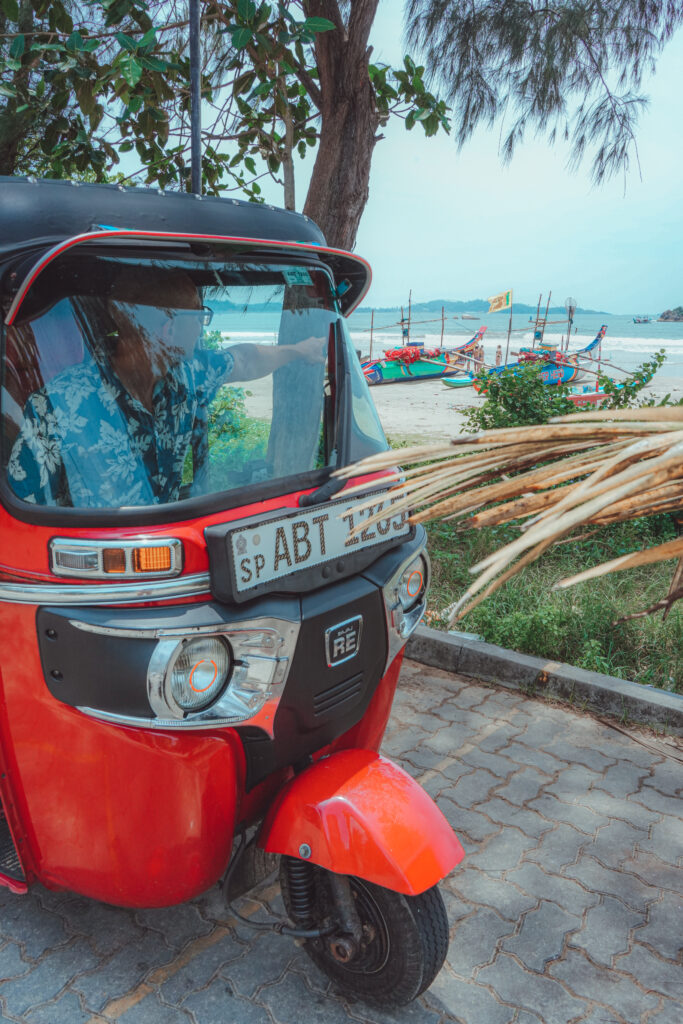 A tuktuk parked on the side of the beach and a man inside it